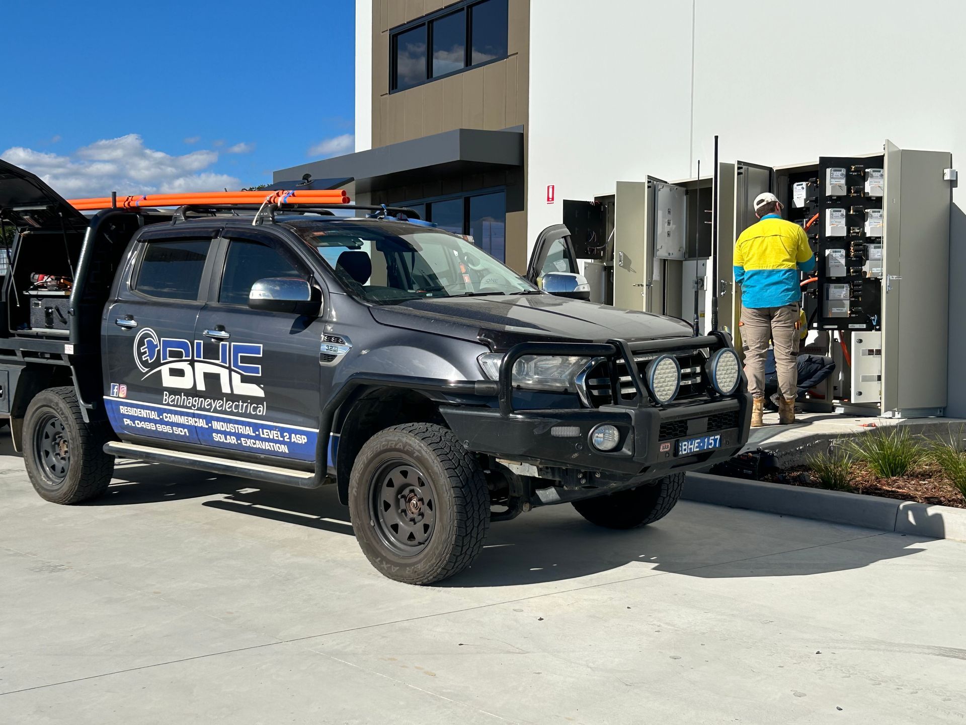 A truck is parked outside a building and a worker in hi-vis vest works on electrical equipment — One Group Industries Pty Ltd in Bathurst, NSW