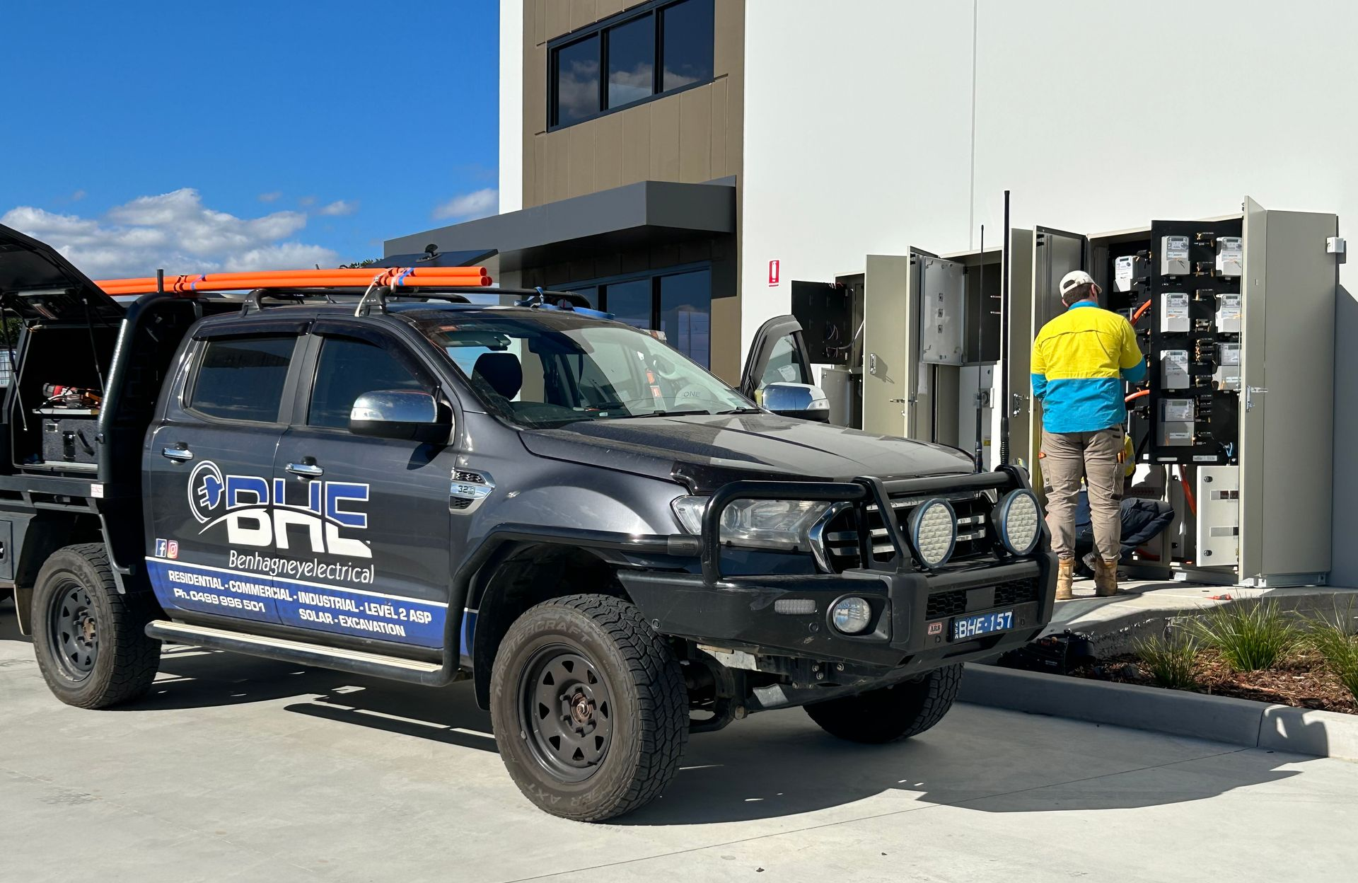 Gray work truck parked beside a building. Electrician in hi-vis working on electrical panel — One Group Industries Pty Ltd in Bathurst, NSW