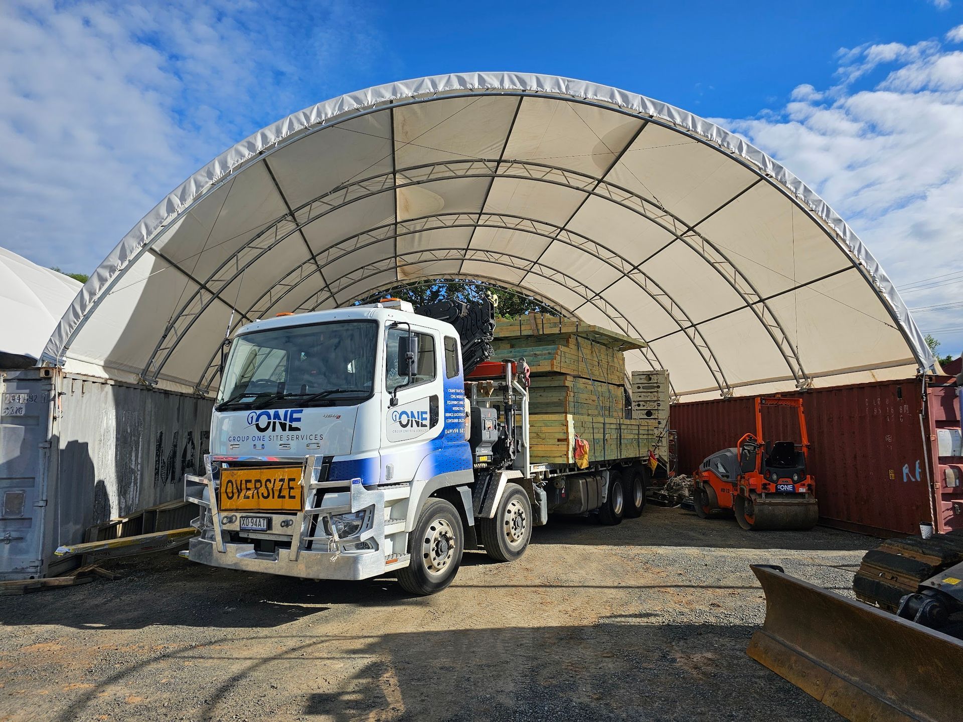 A truck loaded with wood under a white arched shelter on a construction site — One Group Industries Pty Ltd in Bathurst, NSW