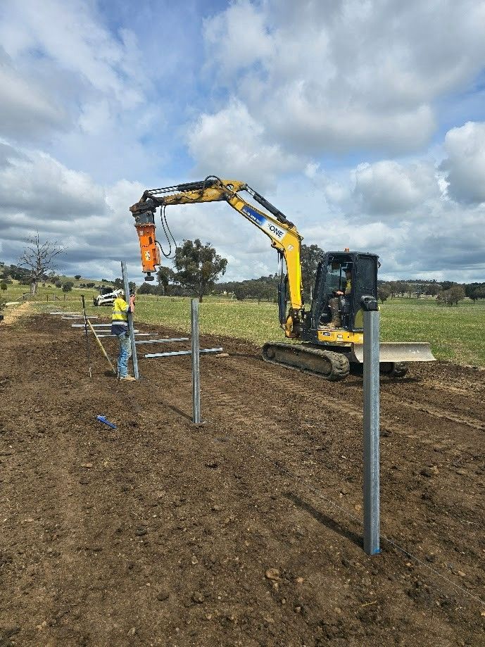 An Excavator Drills Posts Into the Brown Earth Field — One Group Industries Pty Ltd in Bathurst, NSW