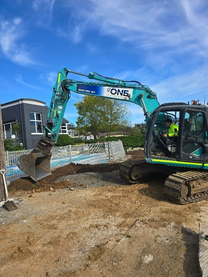 A Teal Excavator Digs Into Dirt Next to A Structure in Front of A Residential House — One Group Industries Pty Ltd in Bathurst, NSW