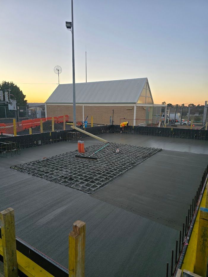 Construction site with concrete slab, grid, and building in the background at sunset — One Group Industries Pty Ltd in Bathurst, NSW