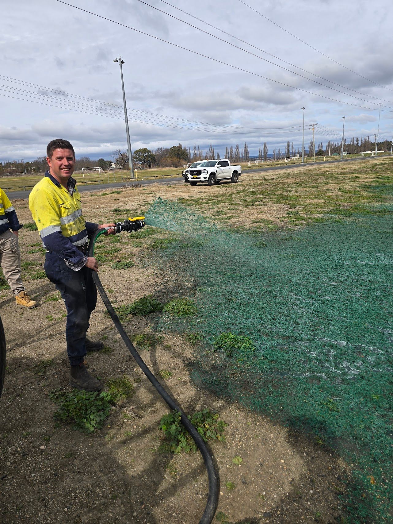 Man in work clothes sprays green liquid on a field, smiling — One Group Industries Pty Ltd in Bathurst, NSW