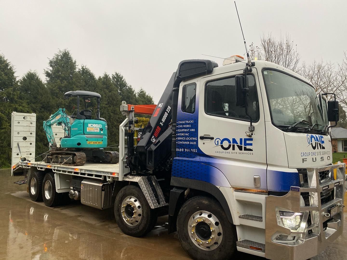A White and Blue Flatbed Truck Carrying a Small Excavator — One Group Industries Pty Ltd in Bathurst, NSW