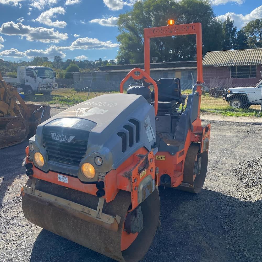 A Gray and Orange Road Roller is Parked in a Gravel Lot — One Group Industries Pty Ltd in Bathurst, NSW