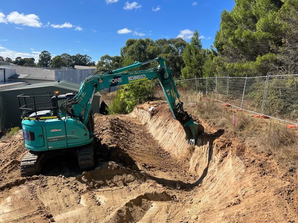 A Green Excavator is Digging a Hole in the Dirt — One Group Industries Pty Ltd in Bathurst, NSW