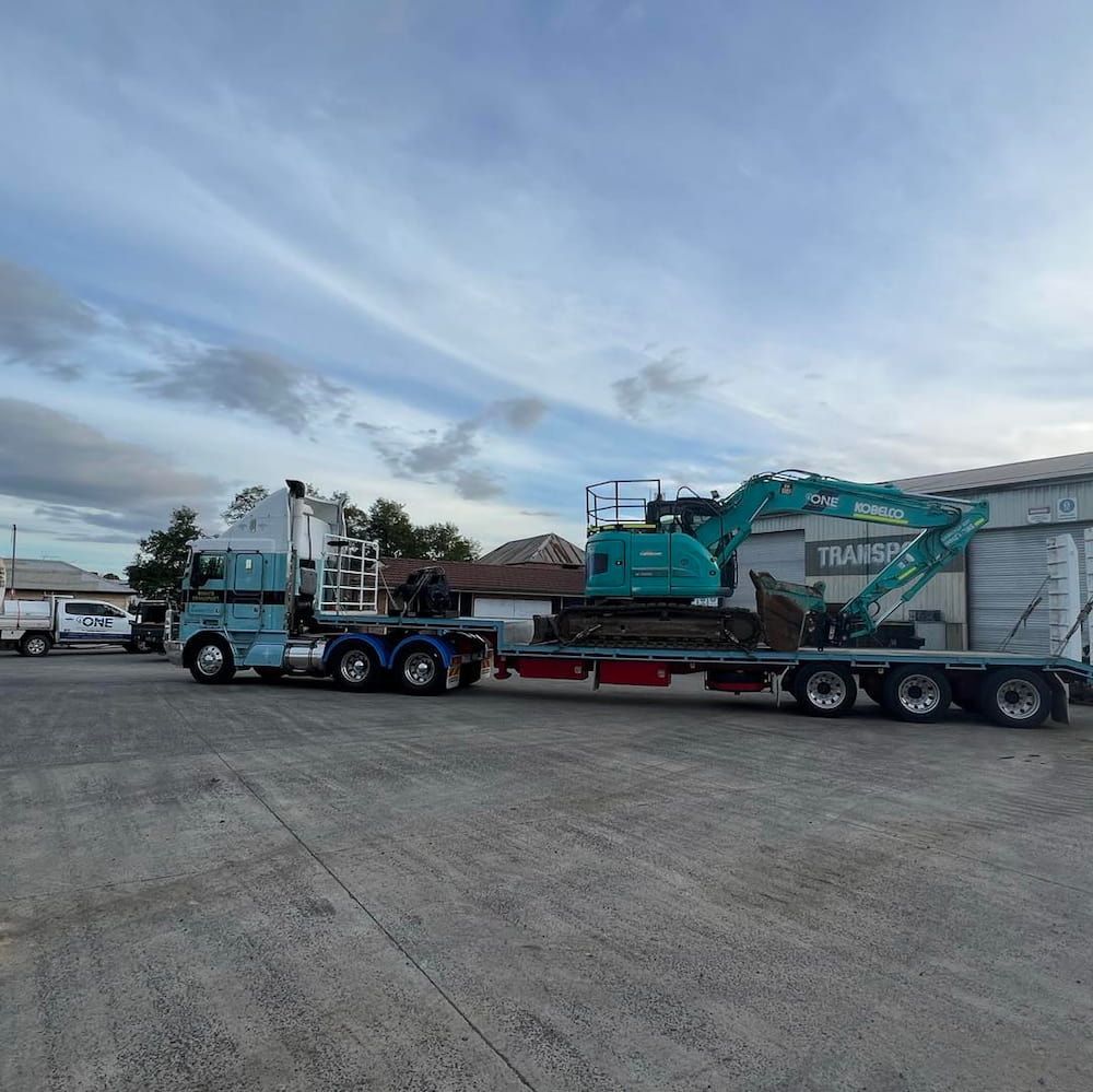 A Blue Semi Truck is Carrying a Green Excavator on a Trailer — One Group Industries Pty Ltd in Bathurst, NSW