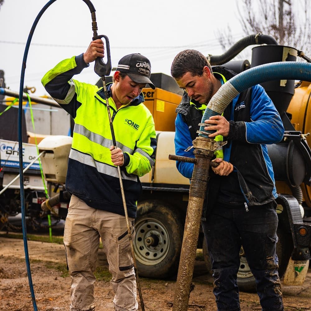 Two workers connect hoses, one in yellow and blue safety gear — One Group Industries Pty Ltd in Bathurst, NSW