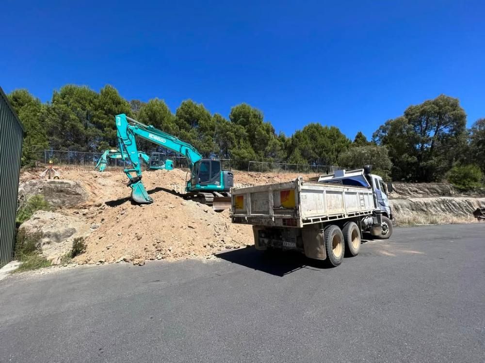 A Dump Truck is Driving Down a Road Next to an Excavator — One Group Industries Pty Ltd in Bathurst, NSW