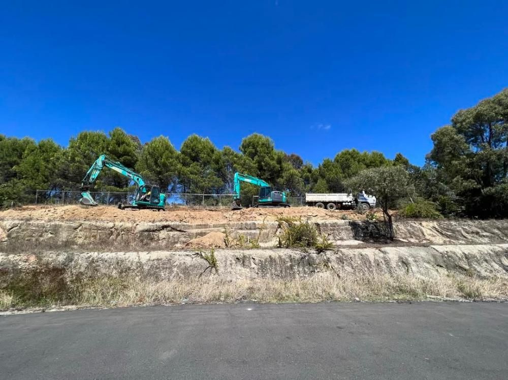 A Couple of Excavators Are Sitting on Top of a Hill Next to a Road — One Group Industries Pty Ltd in Bathurst, NSW