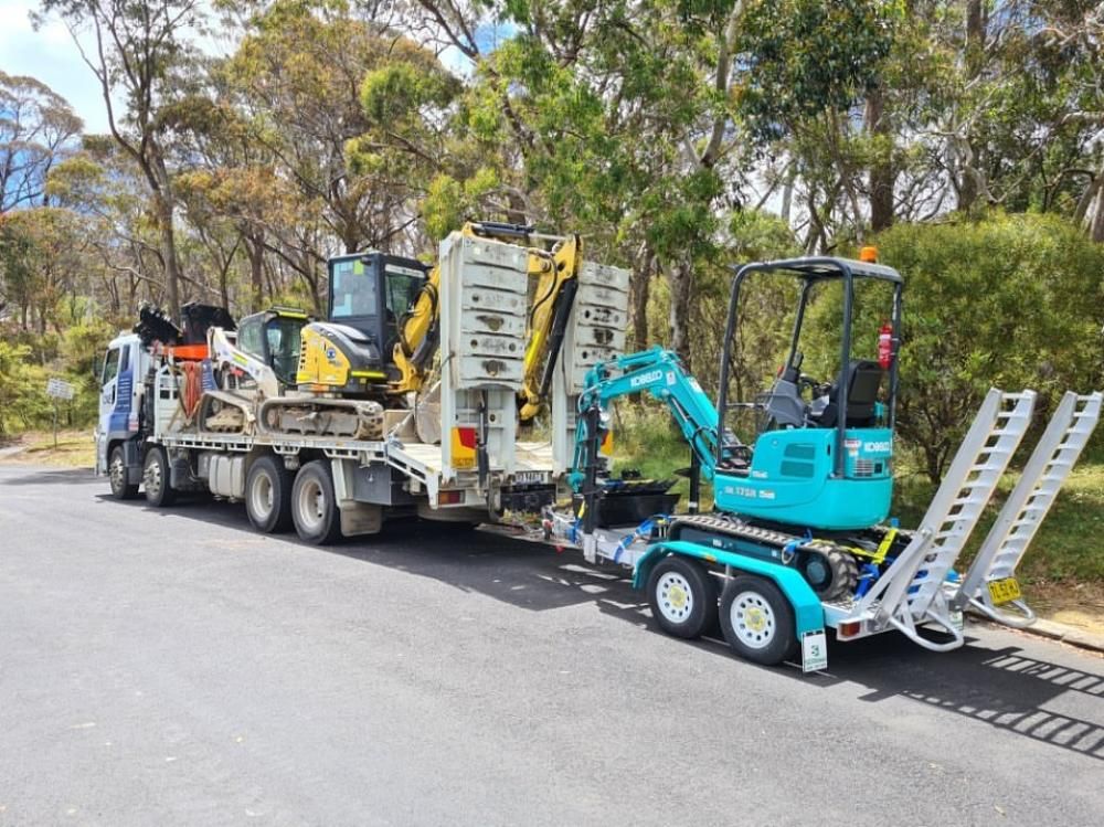 Truck transporting excavators on a road with trees in the background — One Group Industries Pty Ltd in Bathurst, NSW
