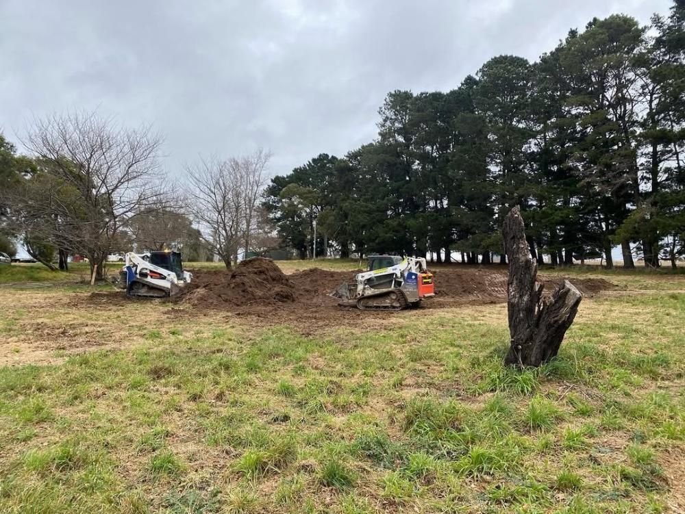 A Bulldozer is Digging a Hole in a Field With Trees in the Background — One Group Industries Pty Ltd in Bathurst, NSW