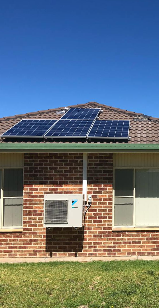Solar panels on a brown-tiled roof above a brick wall with an air conditioner and windows — One Group Industries Pty Ltd in Bathurst, NSW