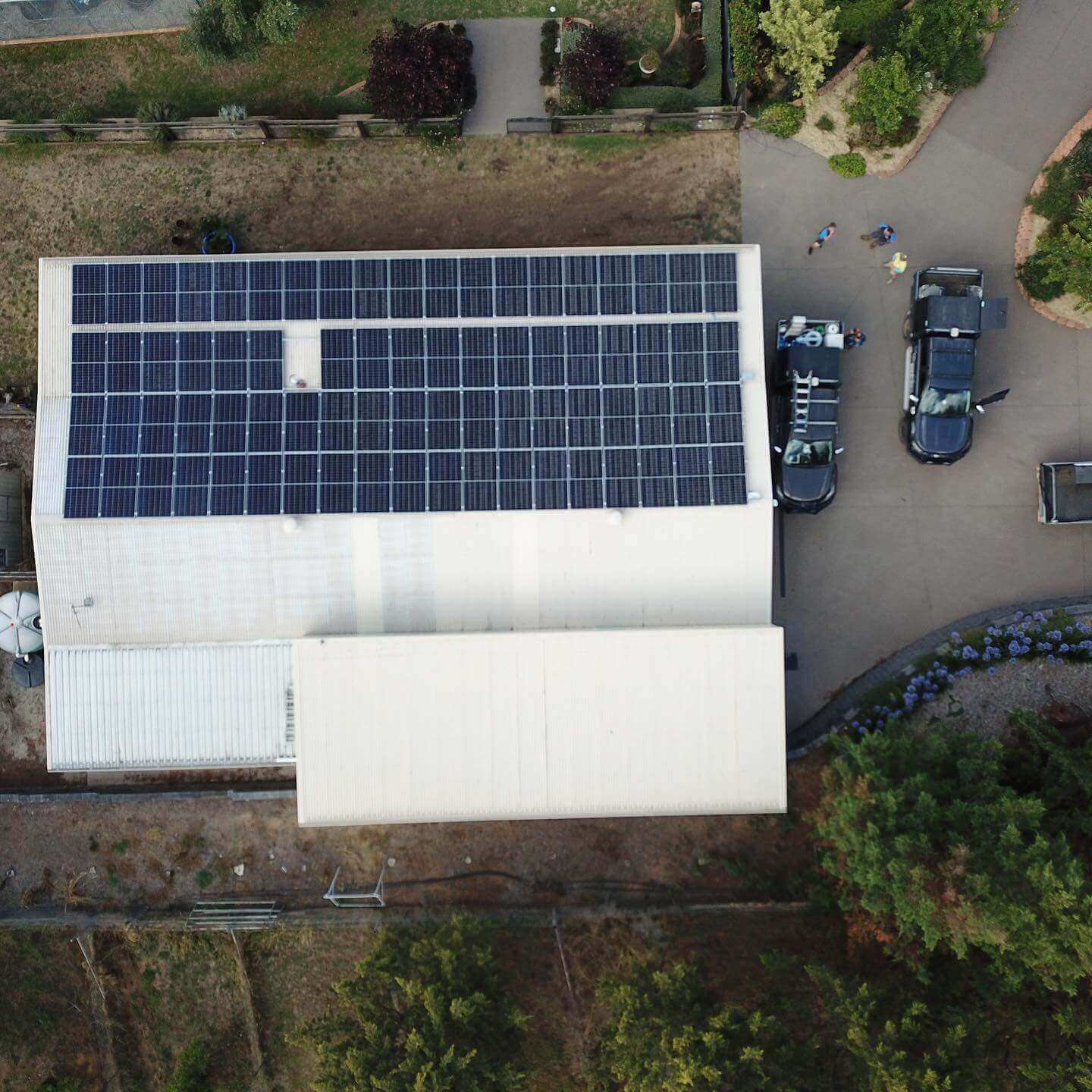 Aerial view of building with solar panels on the roof, two black trucks parked nearby, and surrounding trees — One Group Industries Pty Ltd in Bathurst, NSW