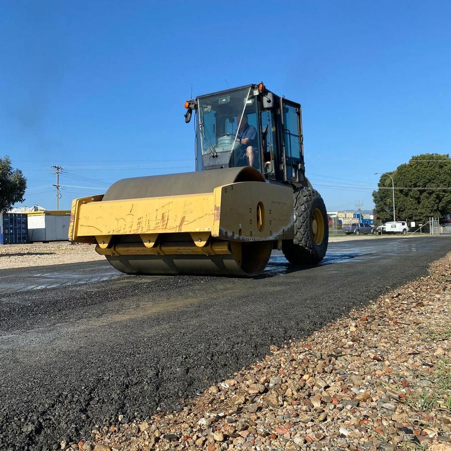 Yellow road roller compacting fresh asphalt on a clear day — One Group Industries Pty Ltd in Bathurst, NSW