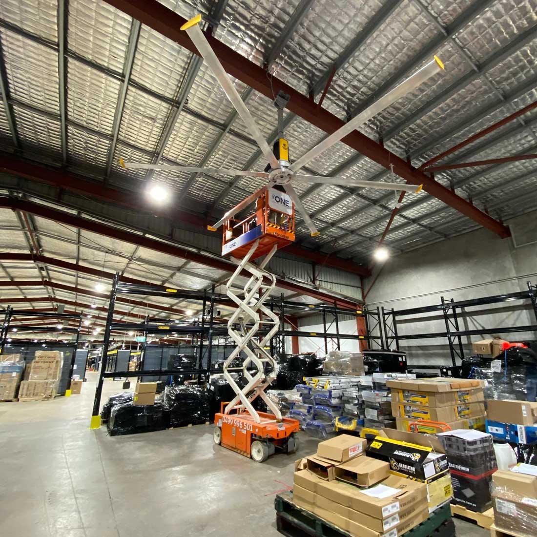Warehouse with a person in a scissor lift working on a large ceiling fan — One Group Industries Pty Ltd in Bathurst, NSW