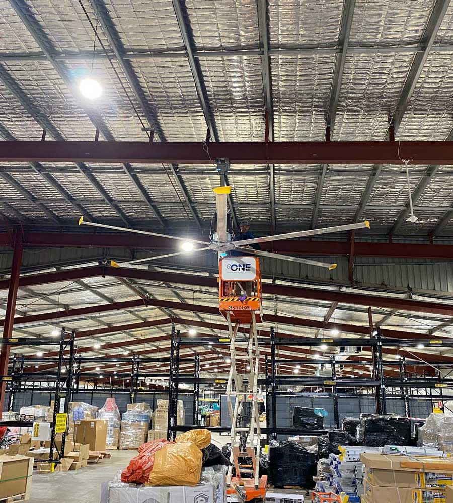 Warehouse with a large ceiling fan, a person in a lift working on the fan — One Group Industries Pty Ltd in Bathurst, NSW