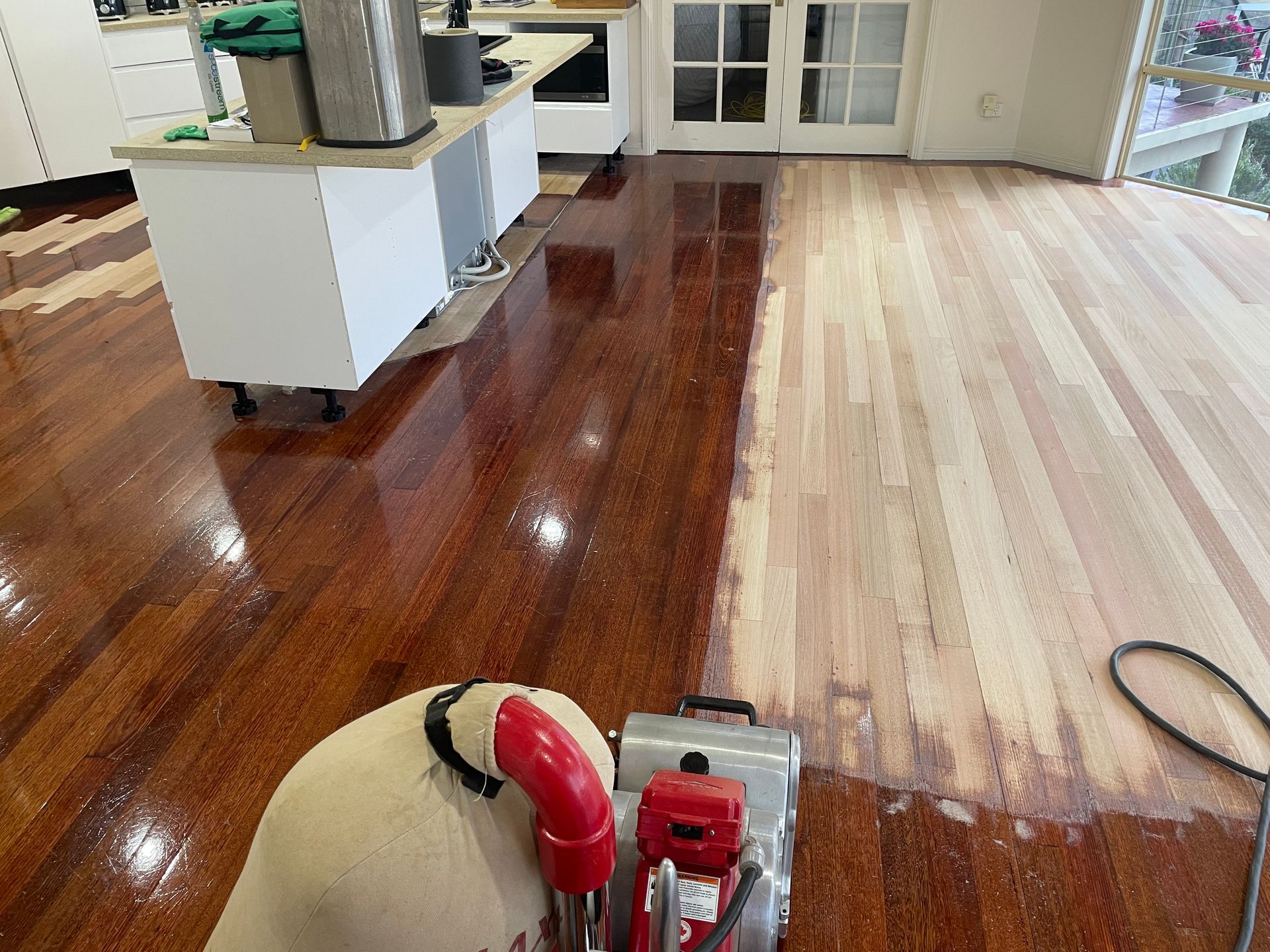 Wood floor being refinished with a sander, showing a glossy dark section beside bare wood. — Finer Floors In Cambridge, TAS