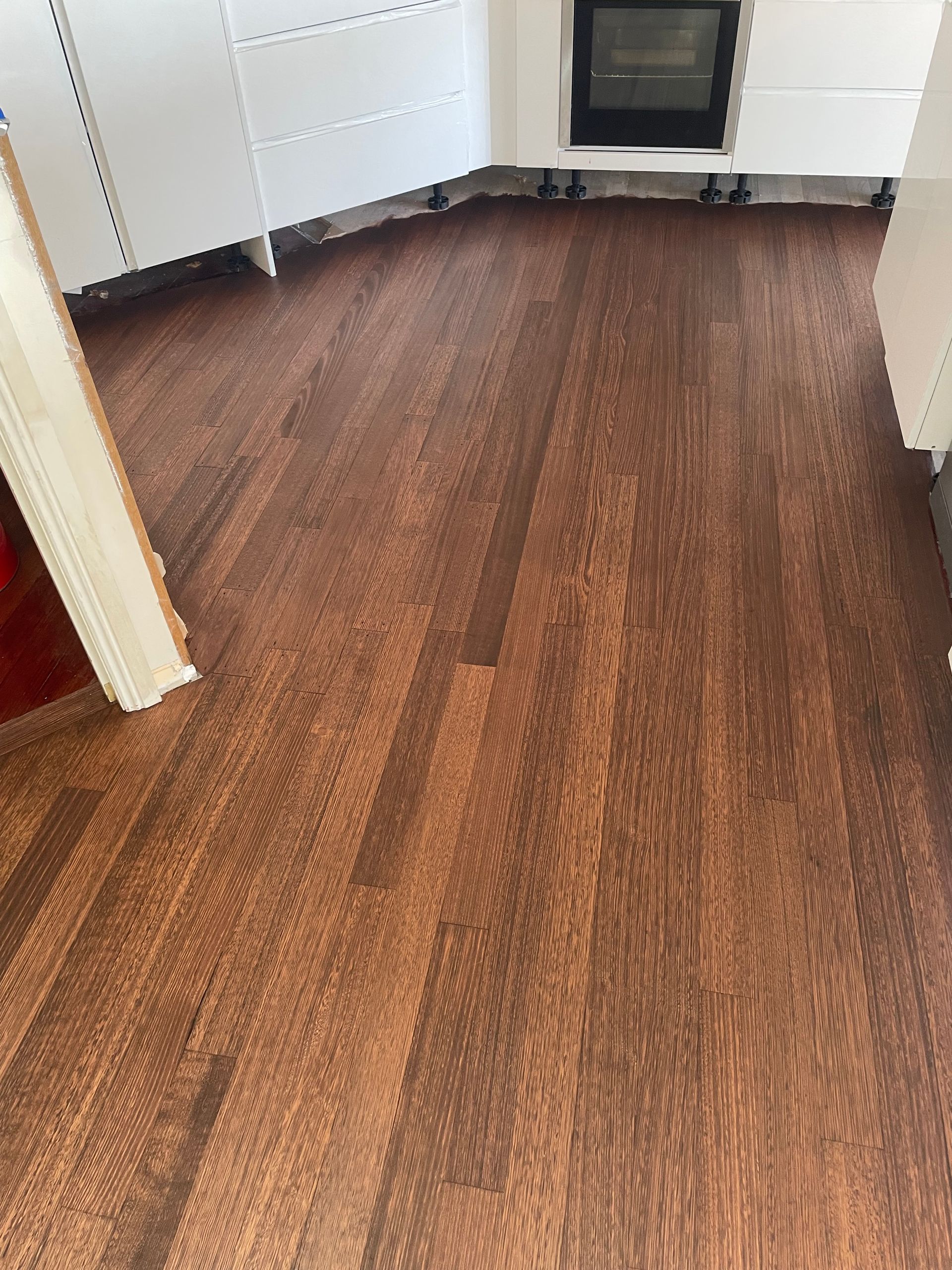 Empty room with brown wood flooring and white walls, viewed through a doorway. — Finer Floors In Cambridge, TAS