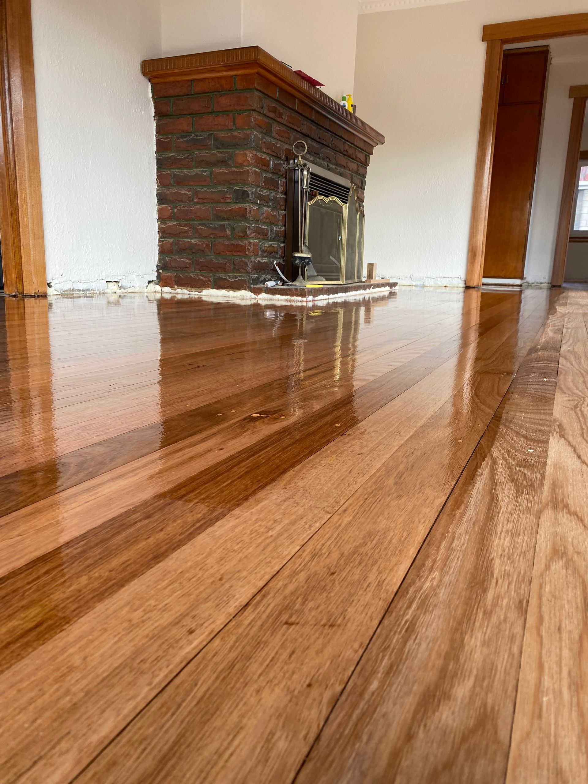 Polished hardwood floors lead toward a brick fireplace in a room with doorway frames.