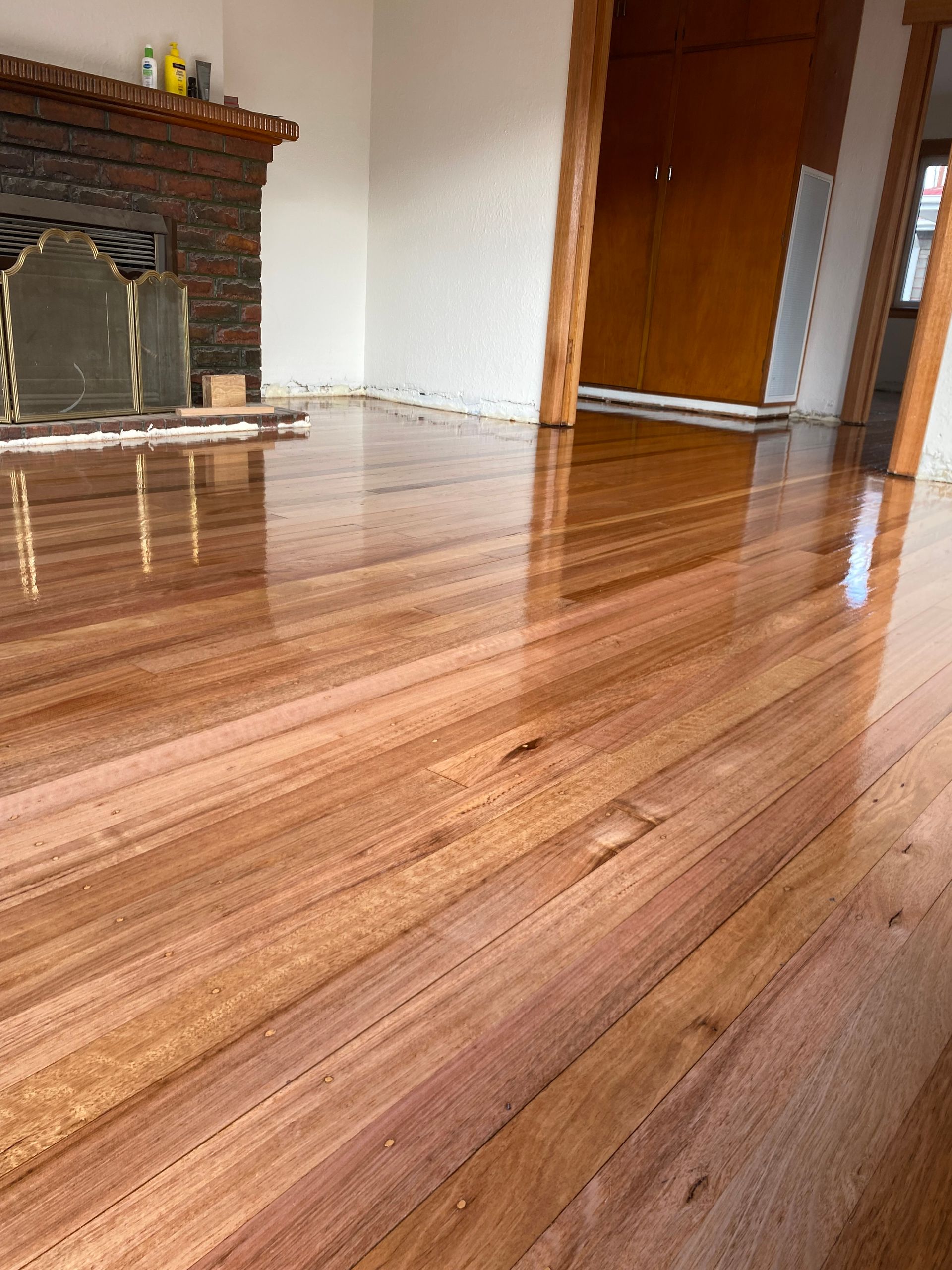 Shiny hardwood floor in a living room with a brick fireplace and wooden door — Finer Floors In Cambridge, TAS