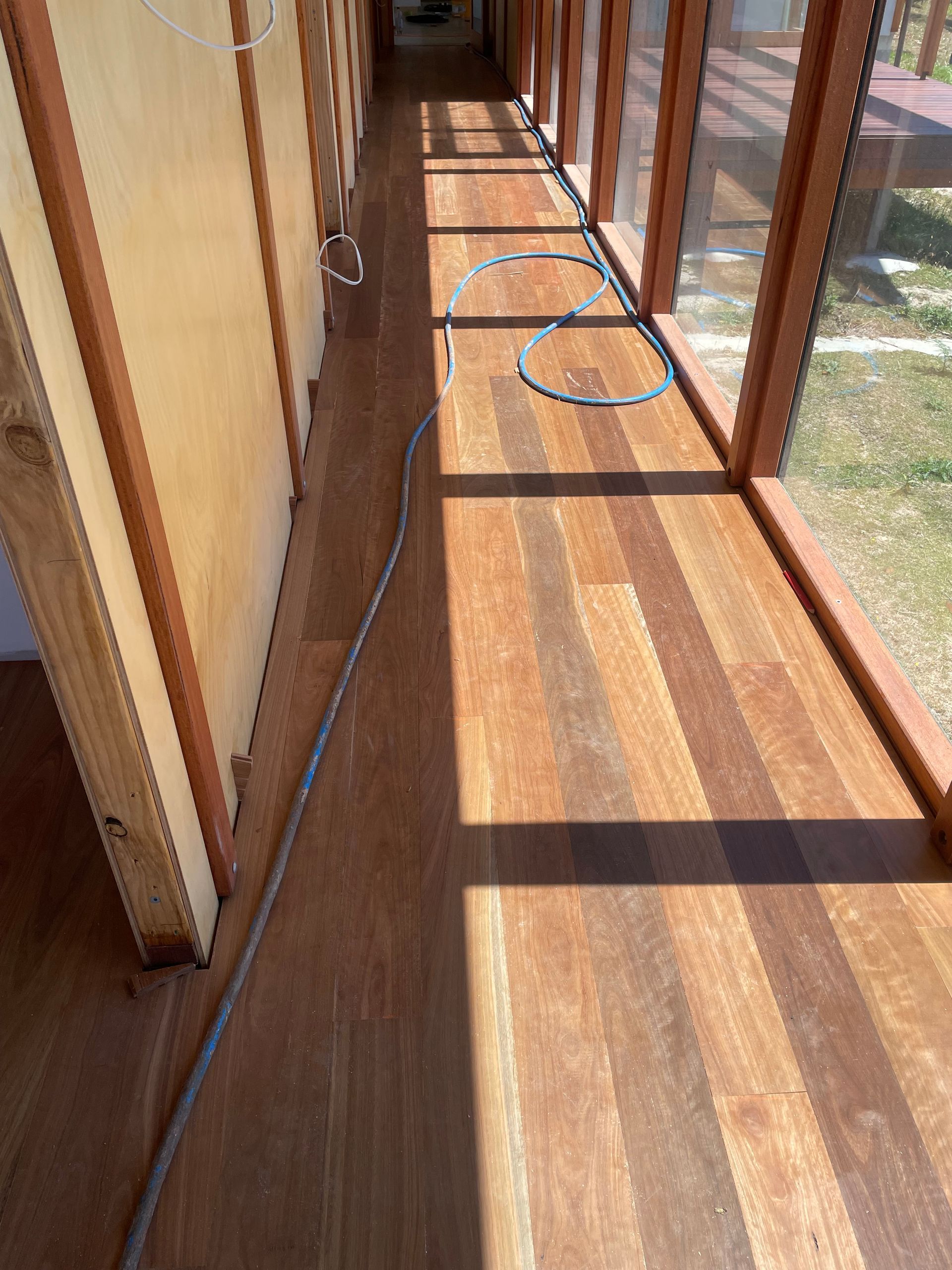 Narrow sunlit hallway with wooden floor, glass doors, and a cable snaking along the walkway — Finer Floors In Cambridge, TAS