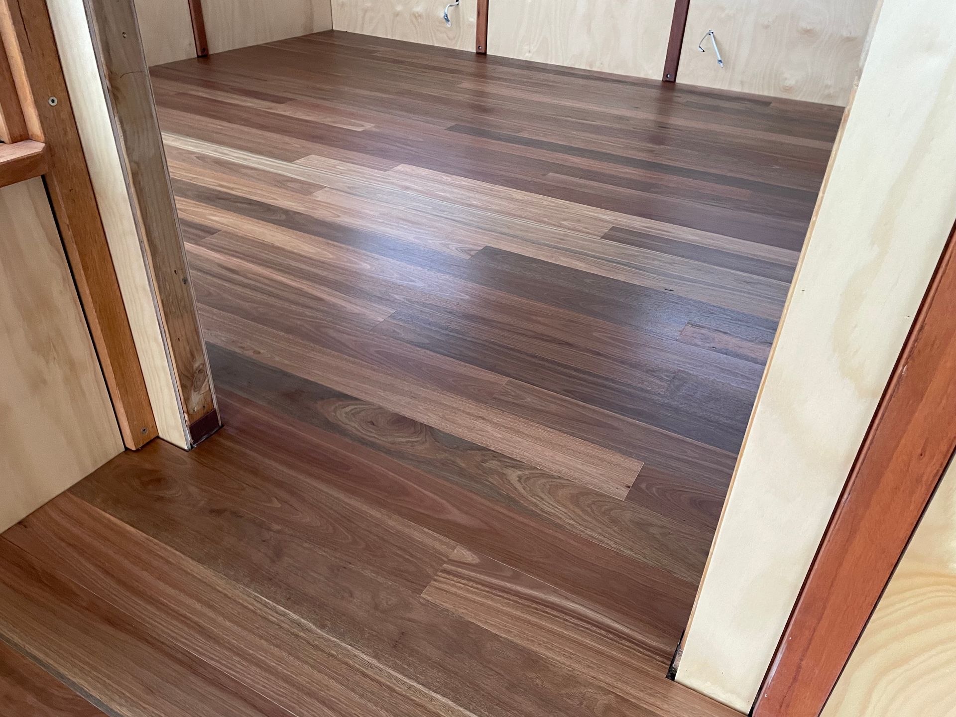Wood-look laminate flooring in a doorway between rooms, with light walls and trim. — Finer Floors In Cambridge, TAS