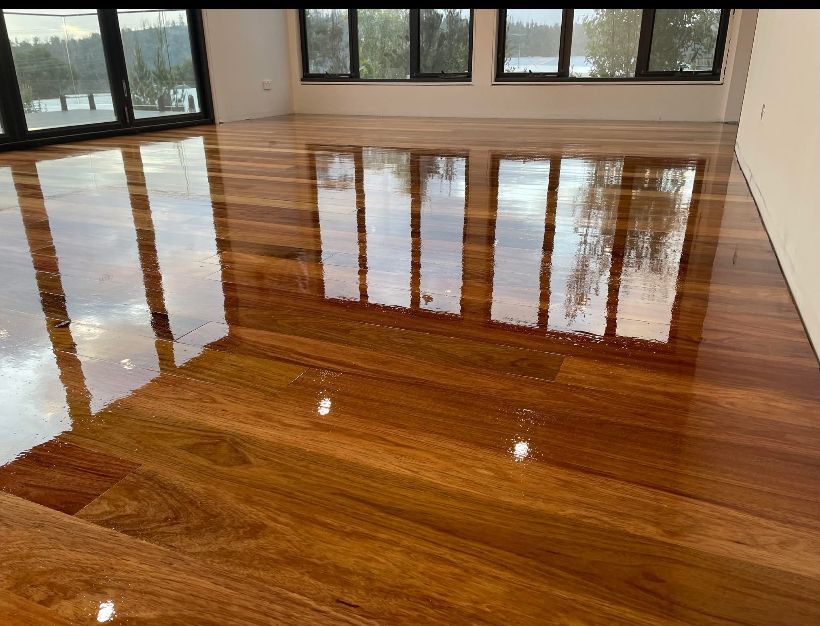 Polished hardwood floor in an empty room, reflecting large windows and overhead lights. — Finer Floors In Cambridge, TAS