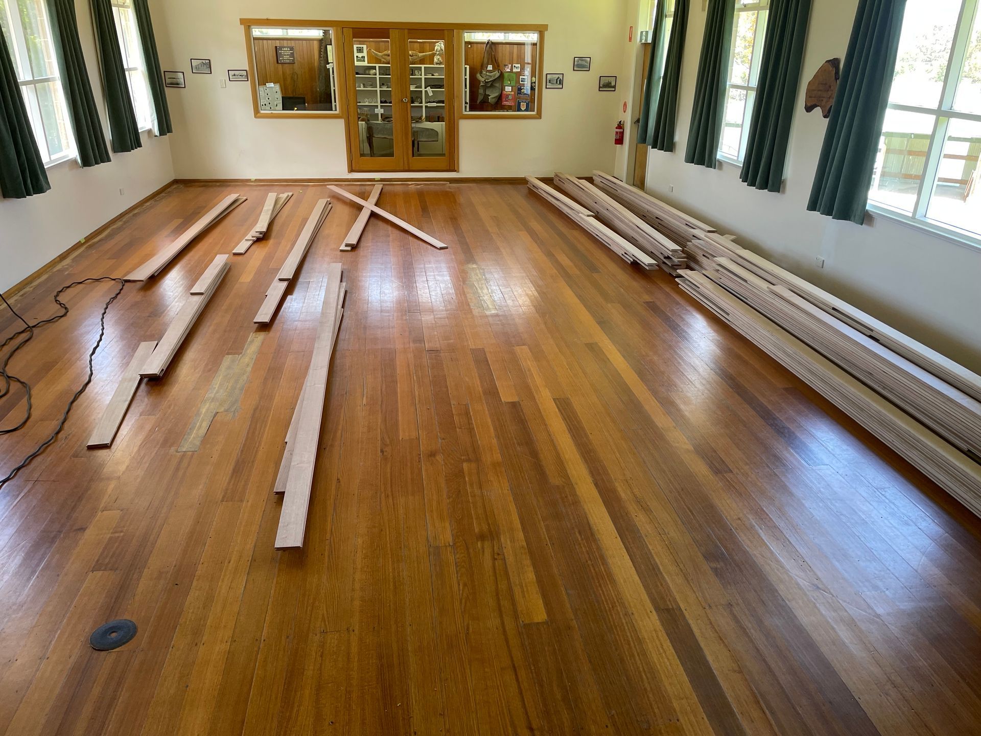 Hardwood floor inside a hall with stacks of construction materials laid out across the centre and right side— Finer Floors In Warrane, TAS