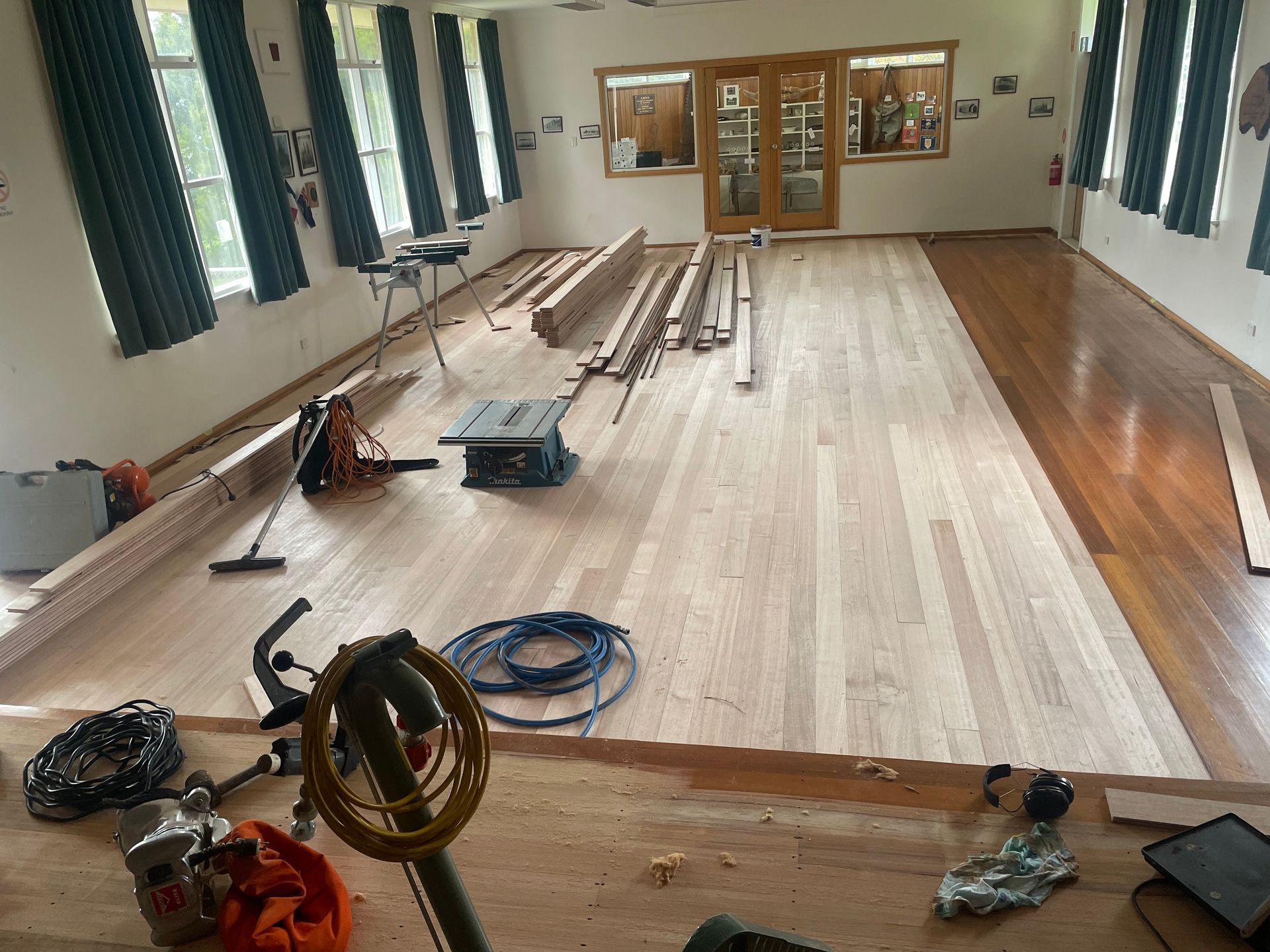 Long hall under renovation with wood flooring, tools, cables, and materials laid out לאורך the room — Finer Floors In Cambridge, TAS