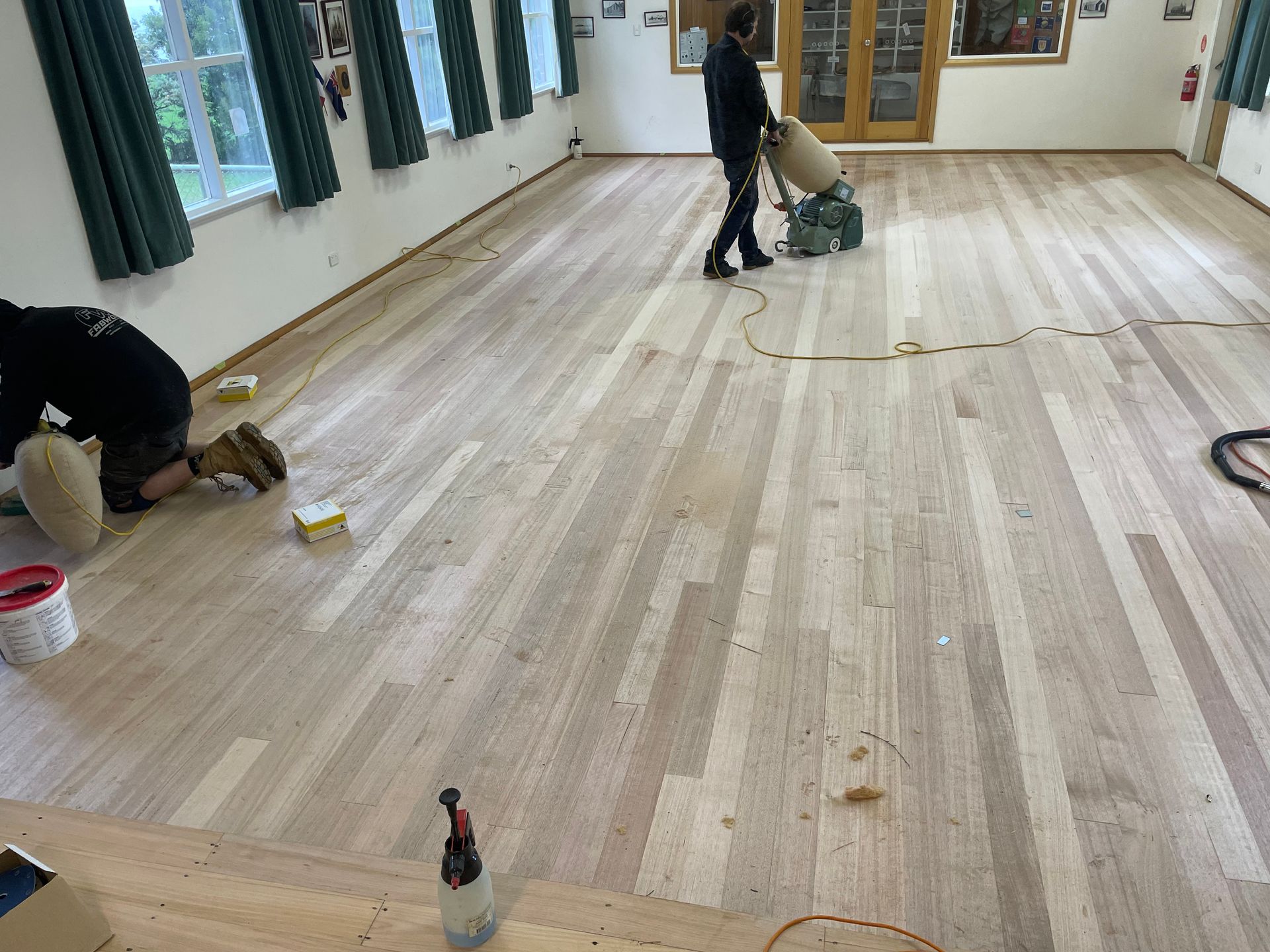 People refinishing a large wooden floor in a bright room — Finer Floors In Cambridge, TAS