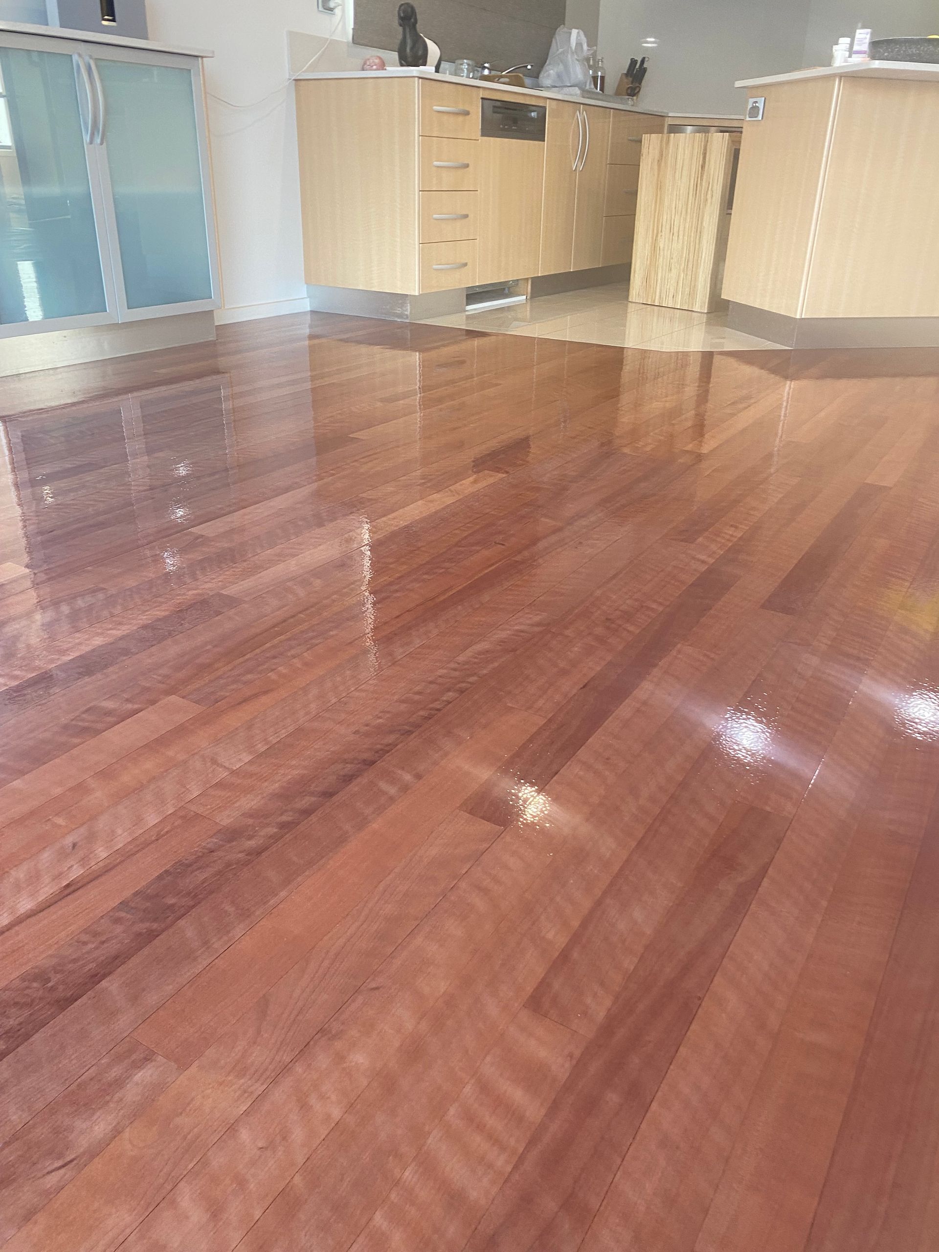 Empty room with glossy wooden floor, cabinet counter, and tall windows in the background. — Finer Floors In Cambridge, TAS