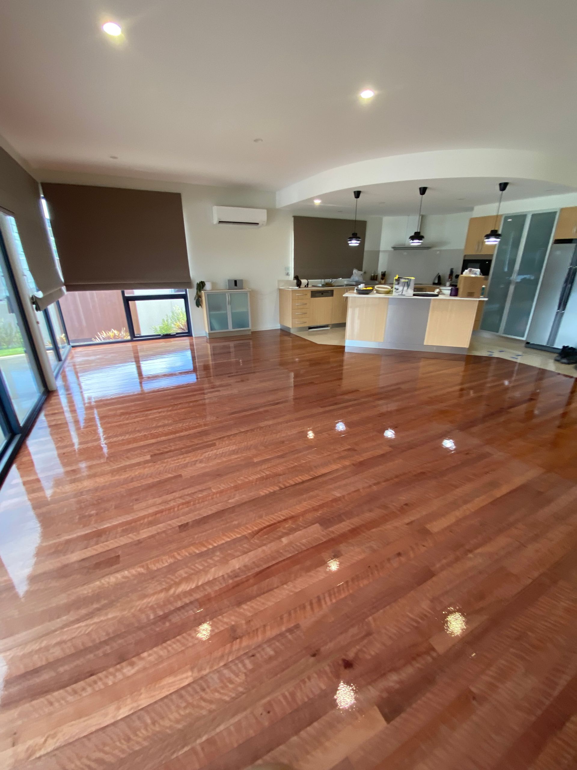 Empty modern living room with glossy wood floors, kitchen island, and large windows. — Finer Floors In Cambridge, TAS