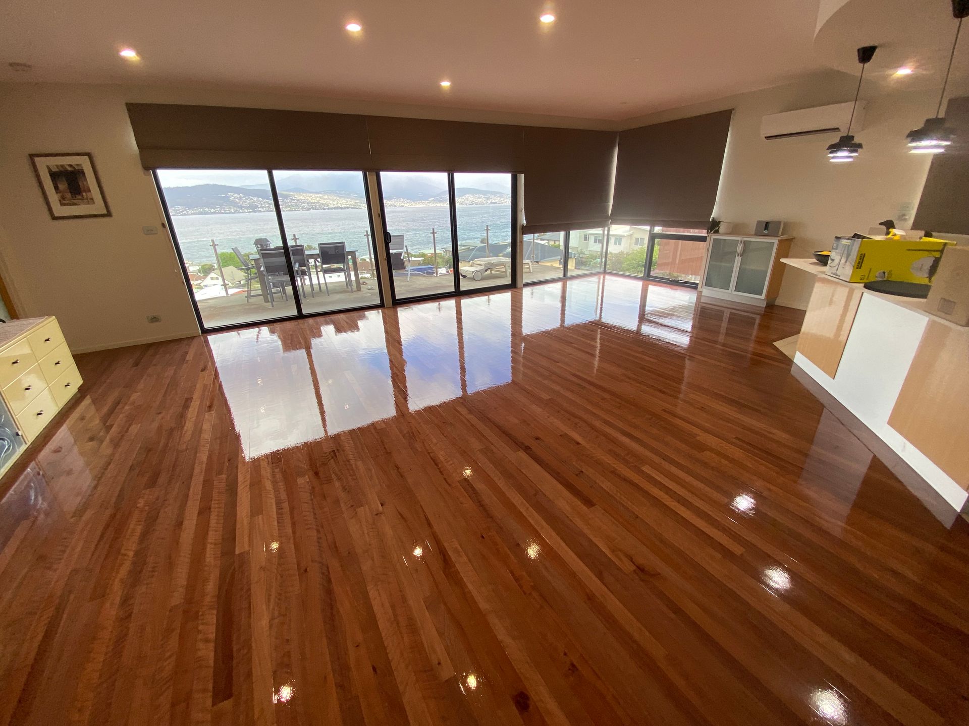 Empty modern living room with polished wood floors, large sliding glass doors, and city views — Finer Floors In Cambridge, TAS