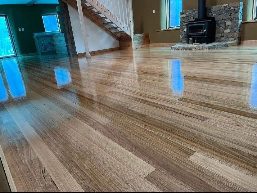 Empty room with glossy wood floor, staircase, and a black wood stove in the corner. — Finer Floors In Cambridge, TAS