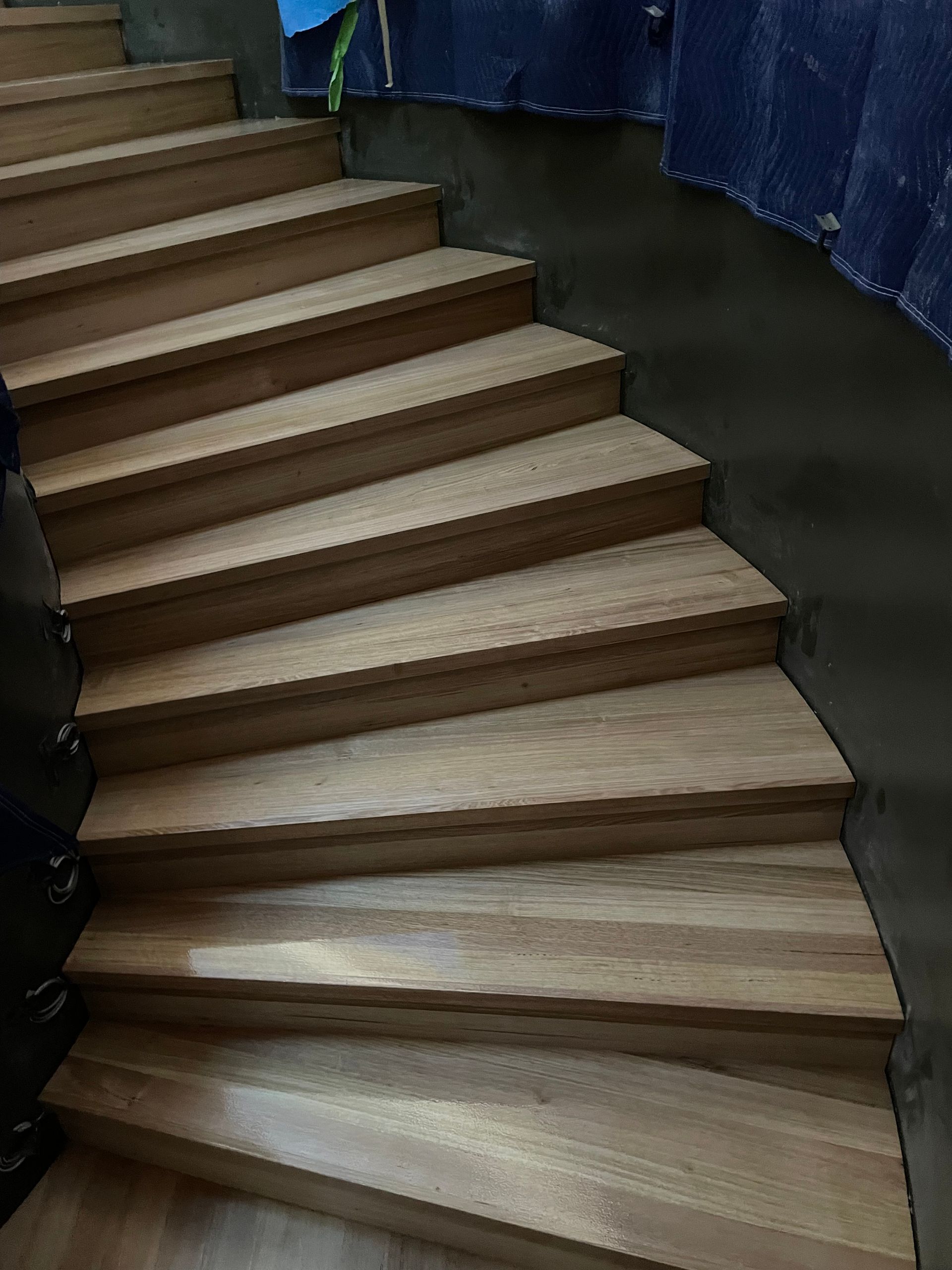Curved indoor staircase with beige wooden steps and blue curtains along the sides. — Finer Floors In Cambridge, TAS