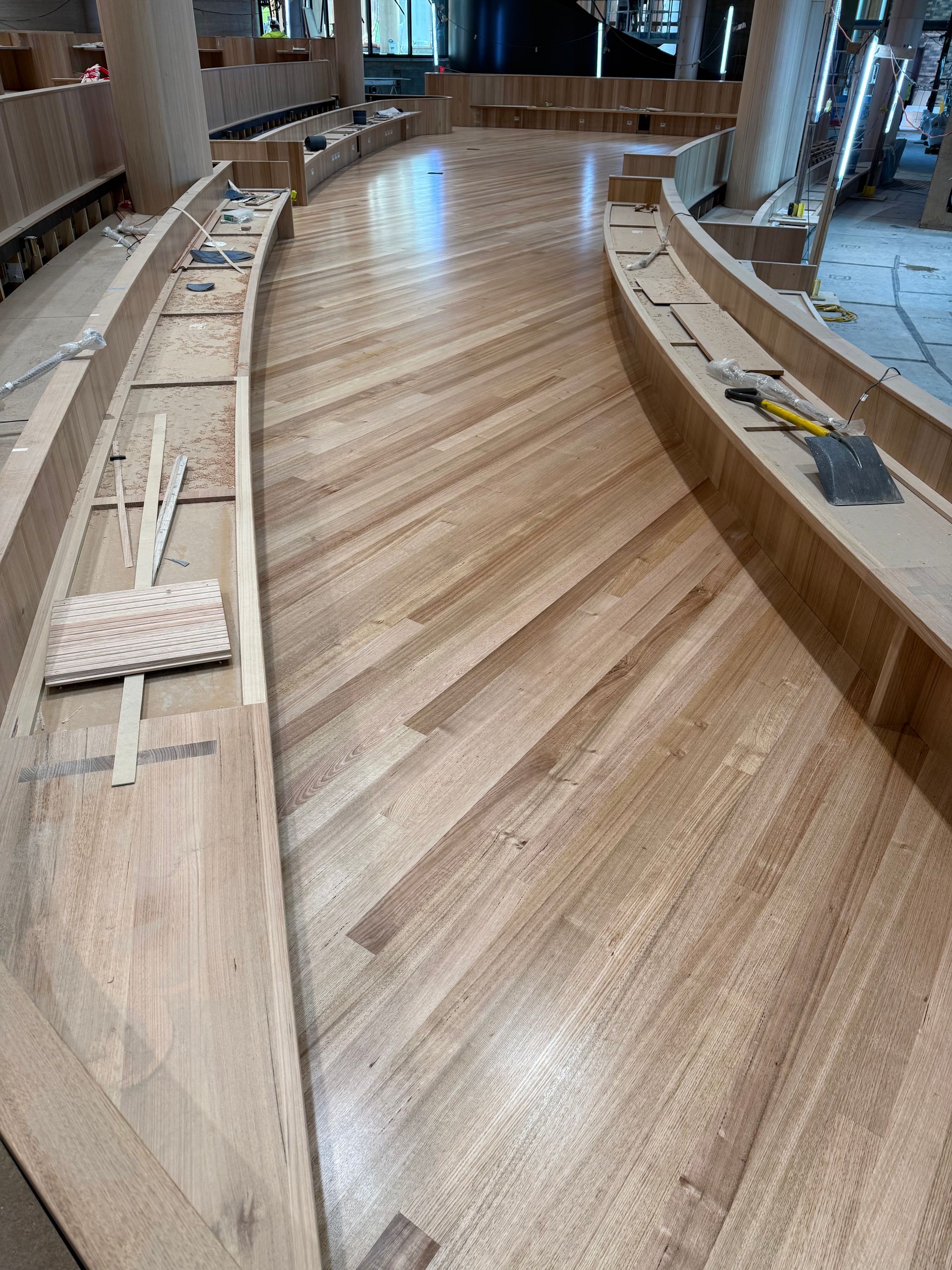 Curved wooden seating or stage construction in a large interior space with a striped wood floor — Finer Floors In Cambridge, TAS