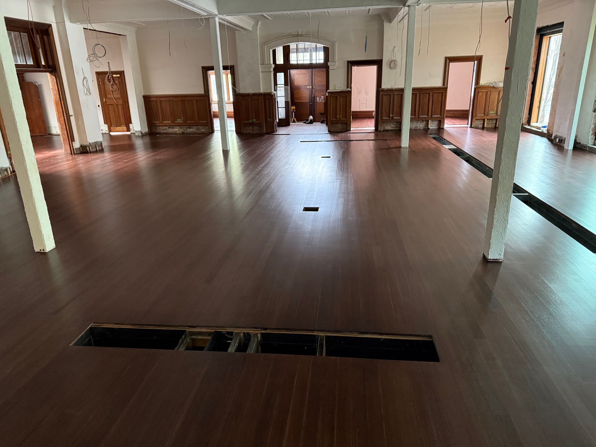 Empty historic hall with polished wooden floor, white columns, and open doorways — Finer Floors In Cambridge, TAS
