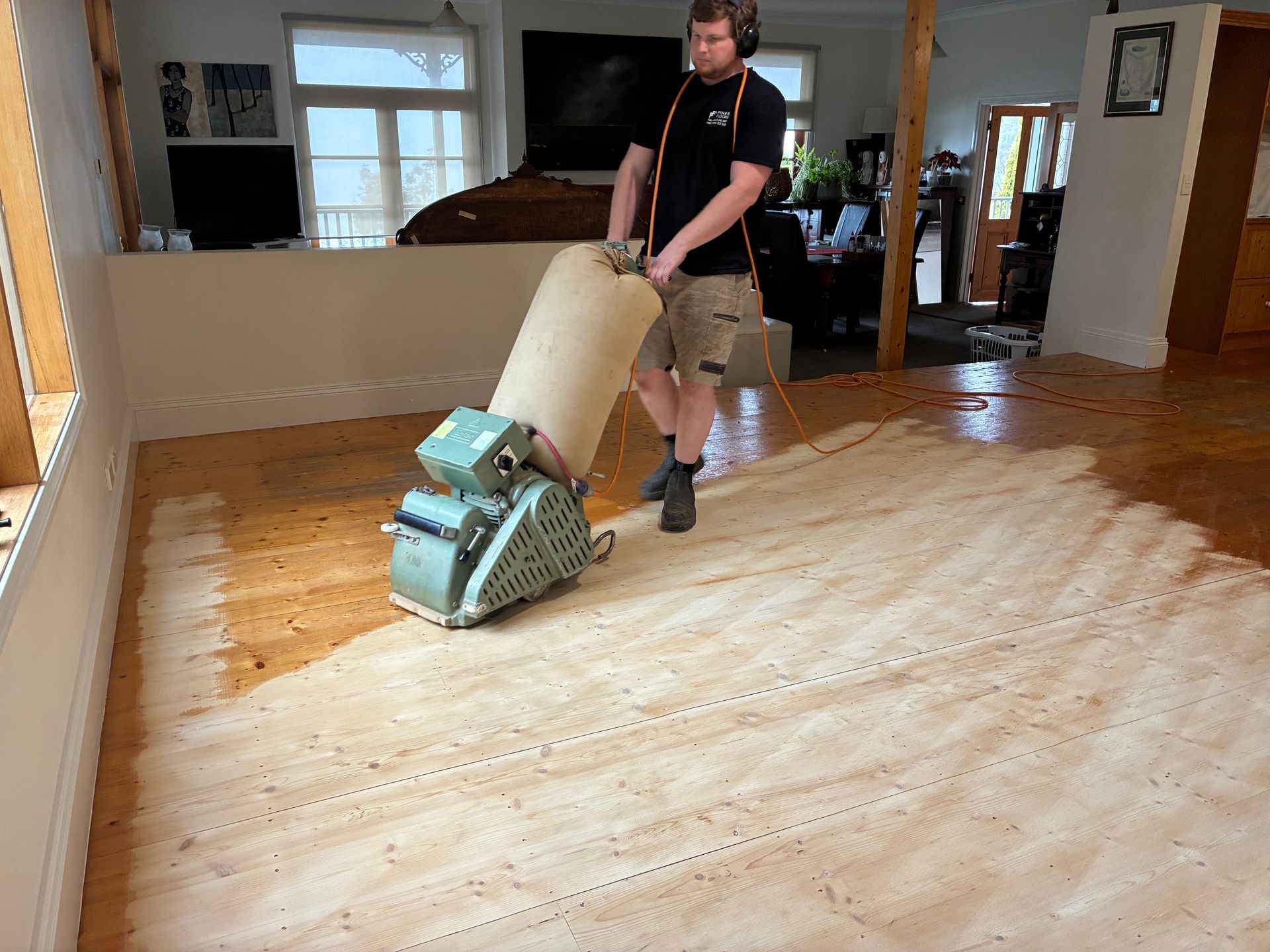 A person using a floor sander on wooden floorboards in a living area.