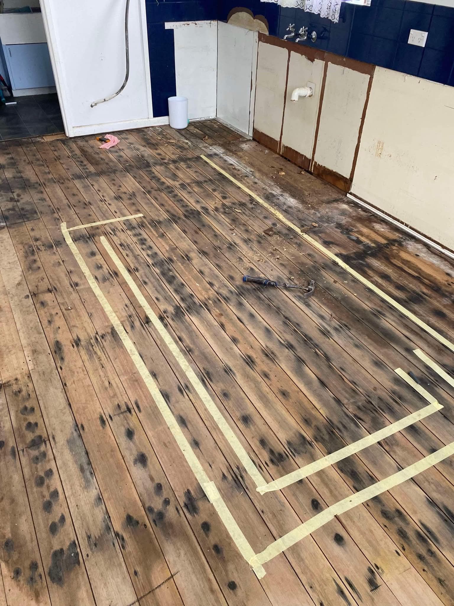 Tape outline on worn wooden floor in a room with white cabinets and a blue wall. — Finer Floors In Cambridge, TAS