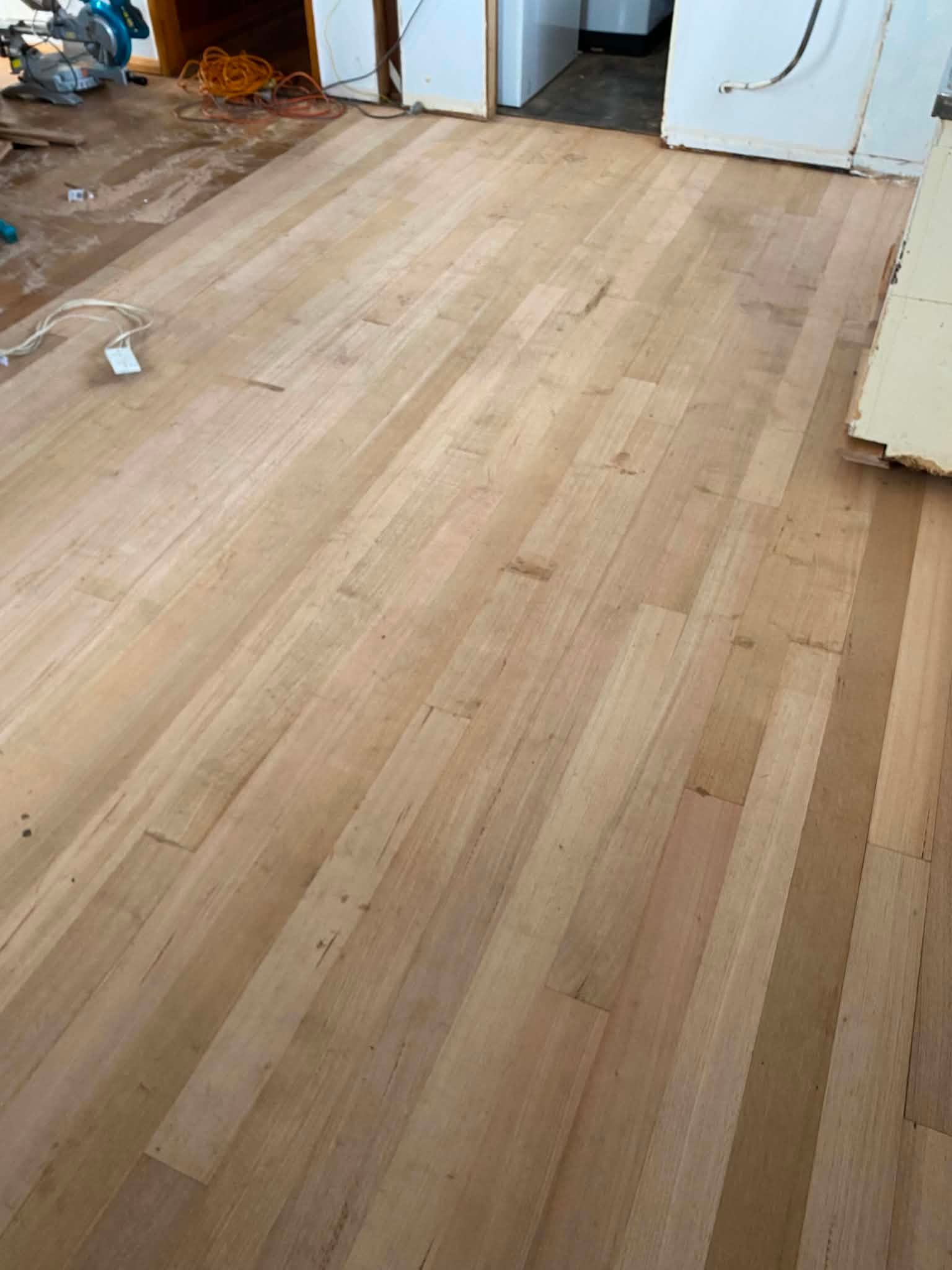 Freshly installed light wood flooring in a room under renovation with tools and debris at the edges — Finer Floors In Cambridge, TAS