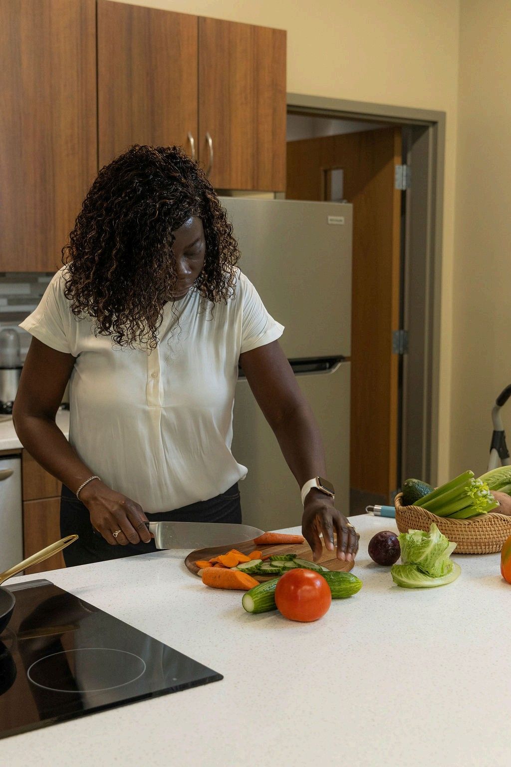 Woman in a kitchen chopping vegetables on a cutting board; various vegetables on the counter.