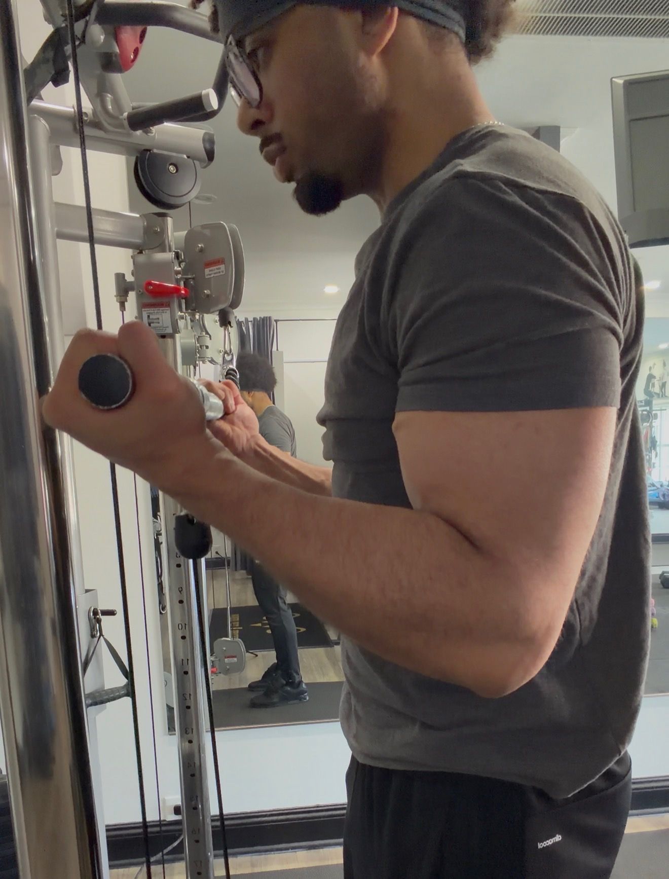 Man doing cable bicep curls in a gym. He is wearing glasses, a grey shirt, and black shorts.
