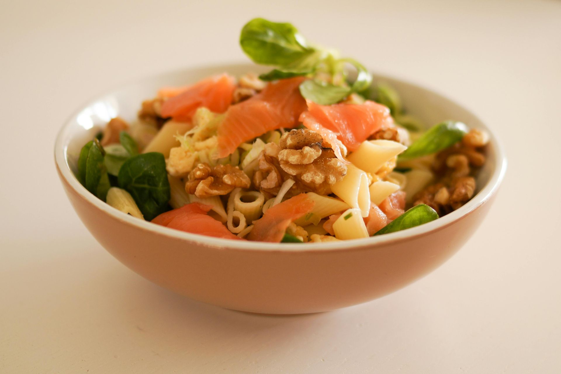 Pasta salad with salmon, walnuts, and greens in a peach-colored bowl.