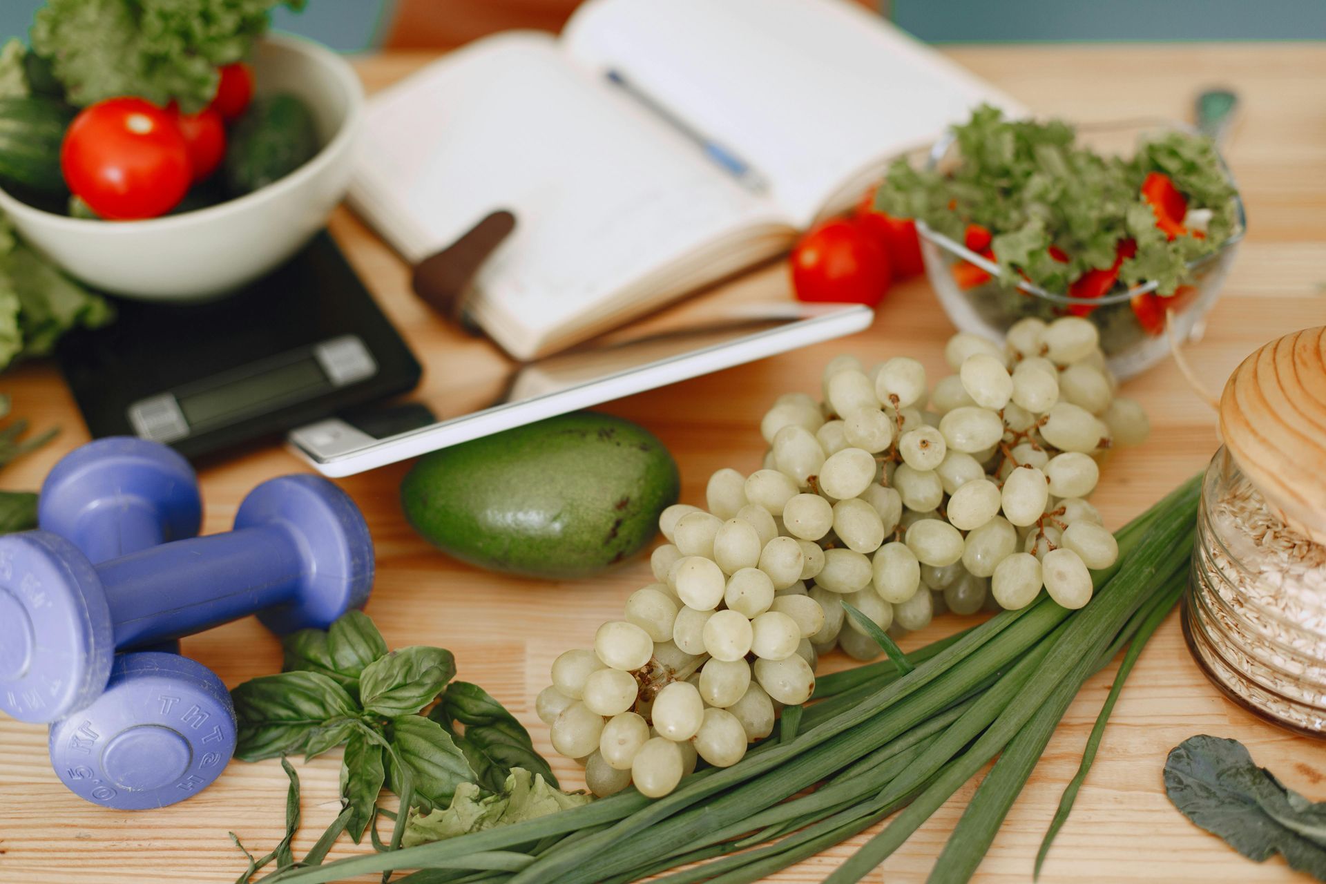 Healthy eating and fitness setup: Vegetables, grapes, weights, notebook on a wooden table.