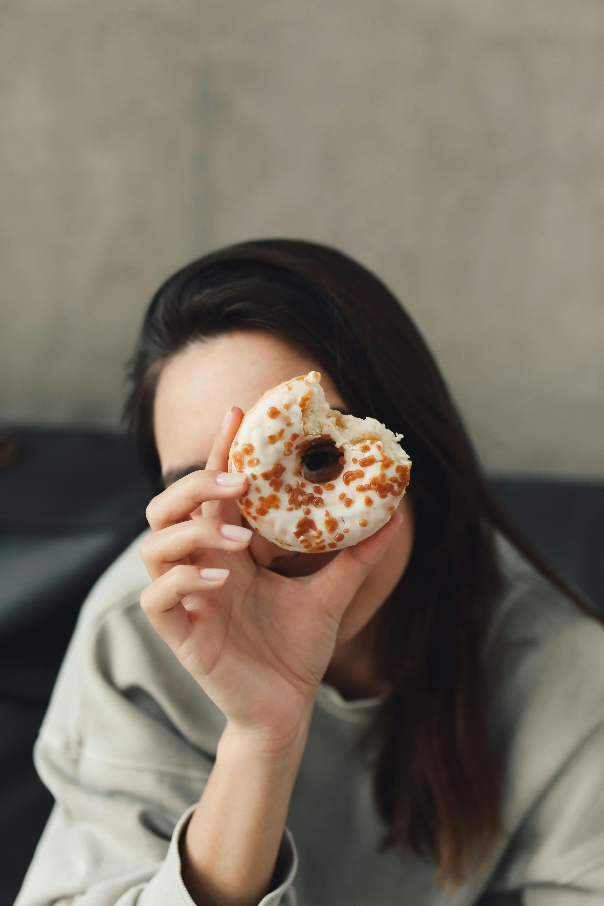 Woman holding partially eaten glazed donut in front of her face.