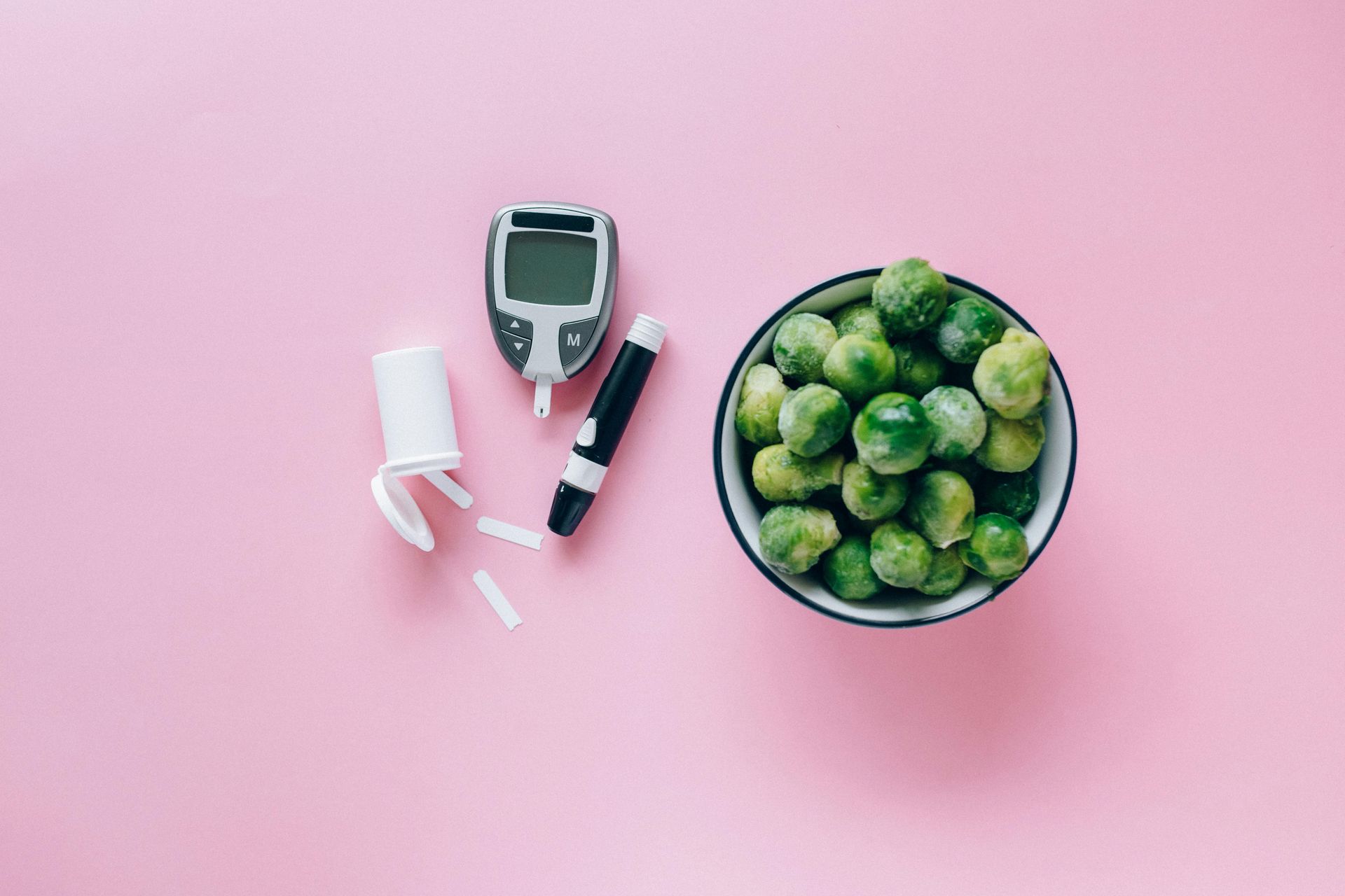 Diabetes supplies and Brussels sprouts on pink surface.