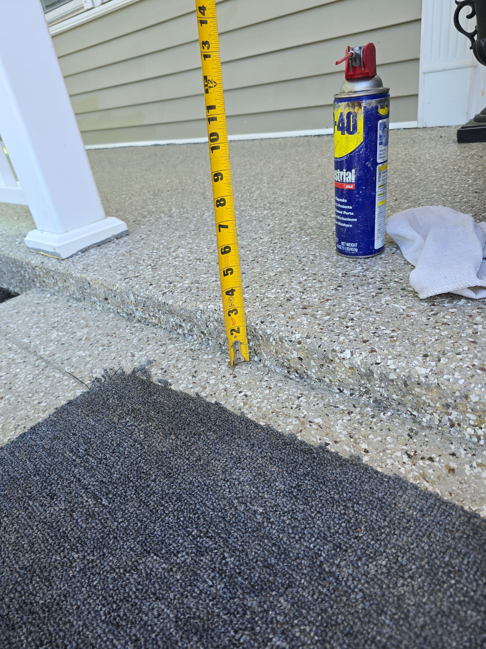 A yellow tape measure positioned vertically next to a front porch step, showing a height of approximately six inches.