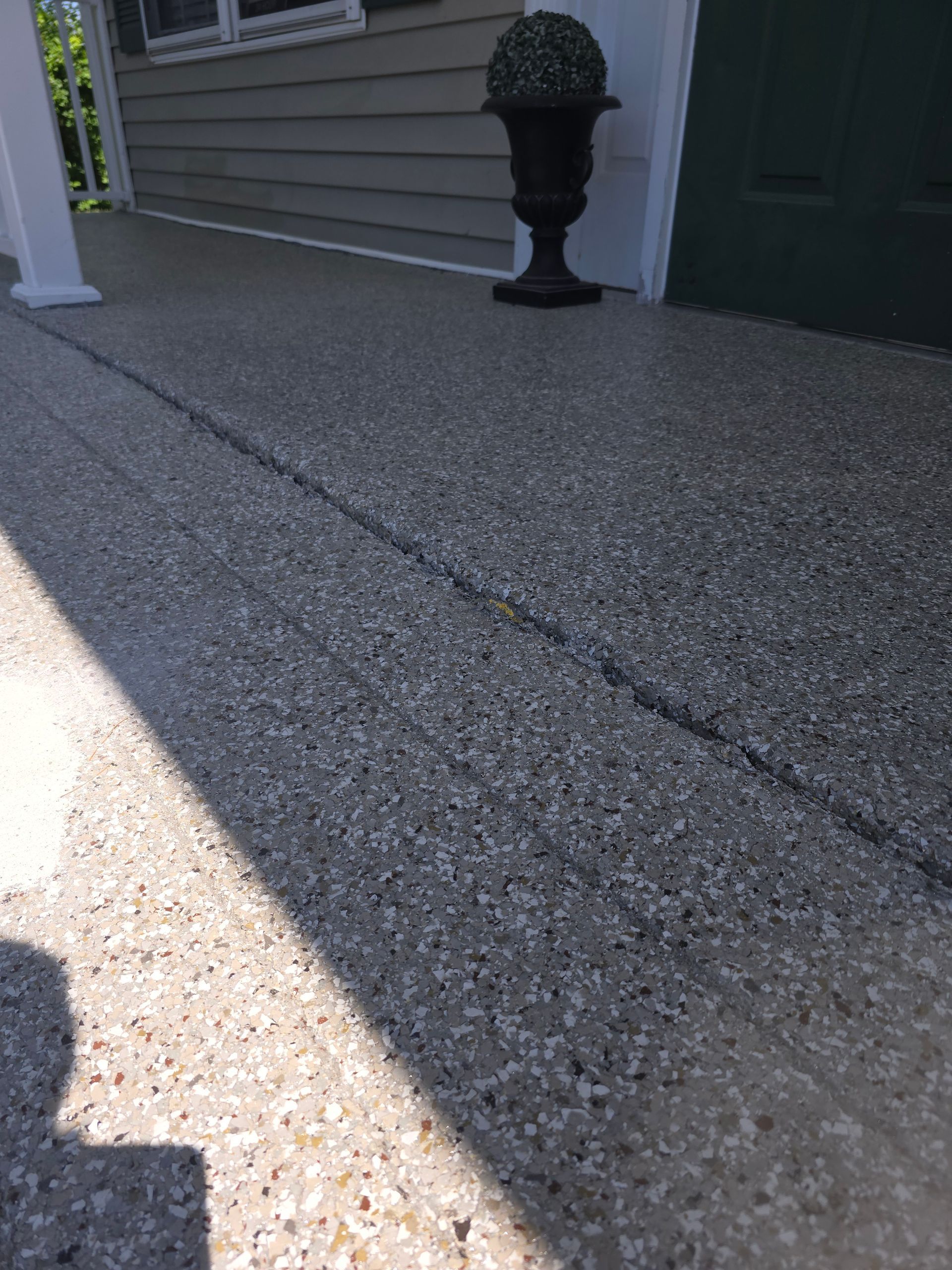 A gray speckled textured porch floor with a black potted plant beside a door, partially in shadow.