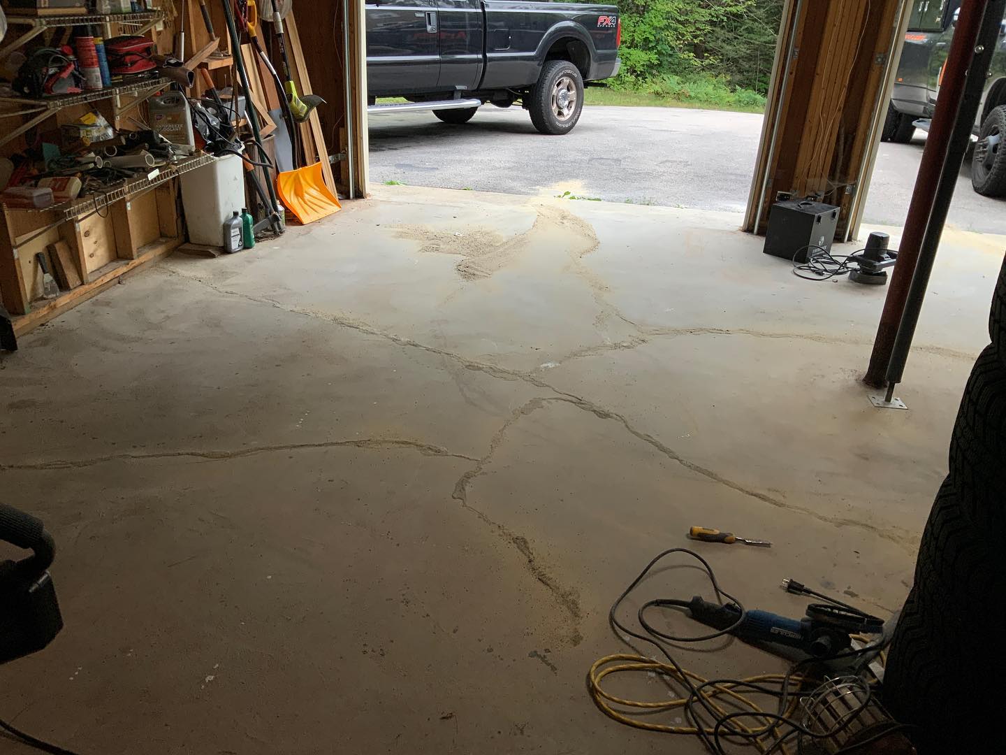 Cracked concrete garage floor with tools, partially visible vehicles, and a cluttered shelf.